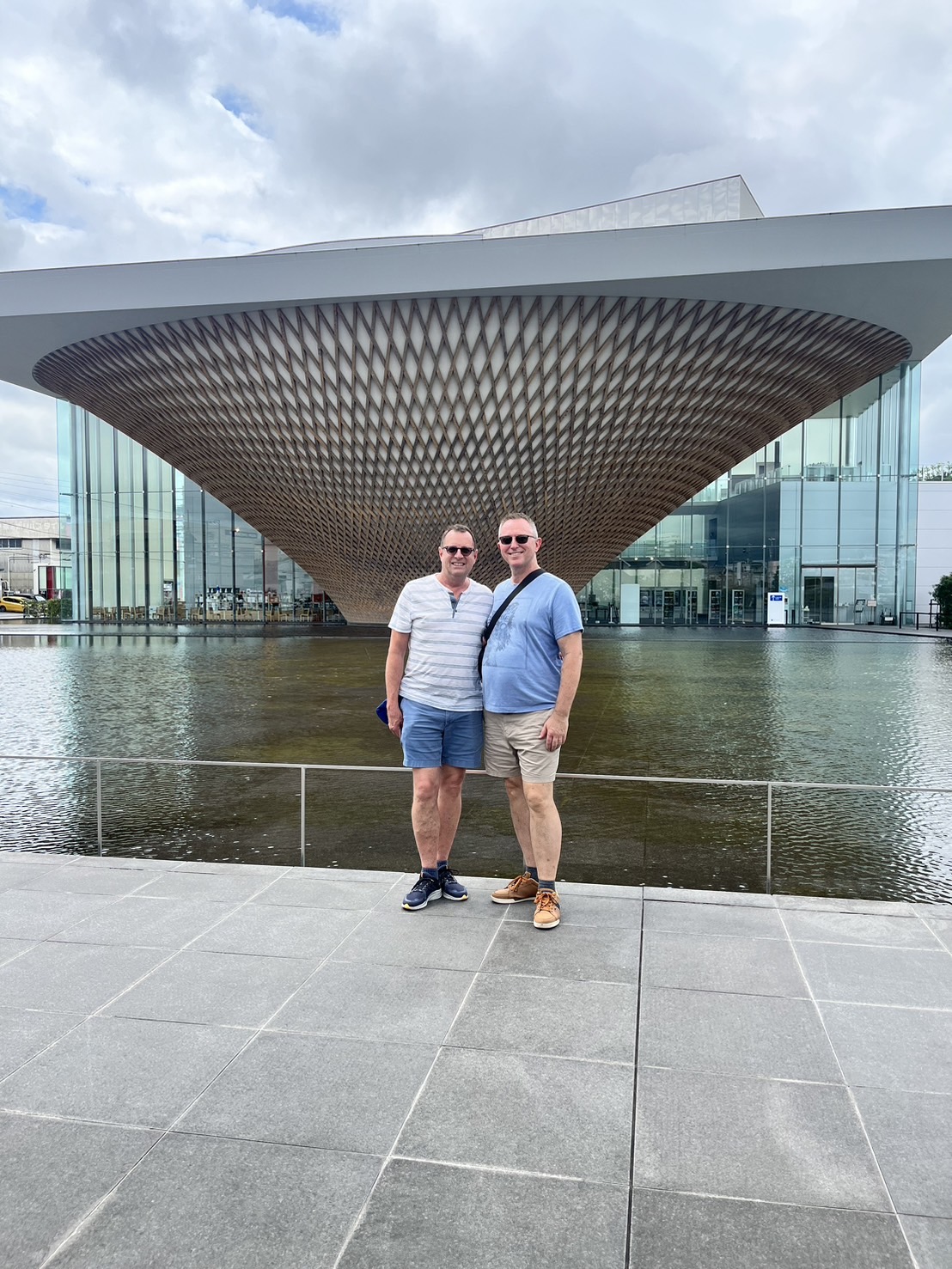 A smiling couple posing in front of the modern Mt. Fuji World Heritage Center building.
