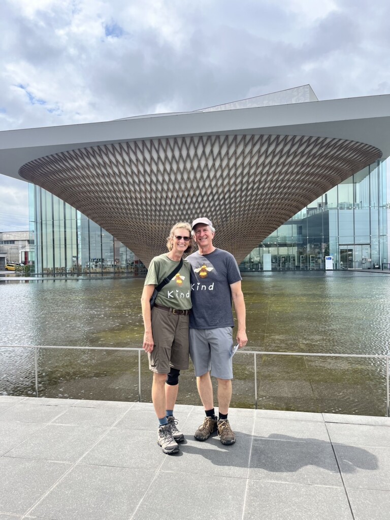 A smiling couple posing in front of the modern Mt. Fuji World Heritage Center building.