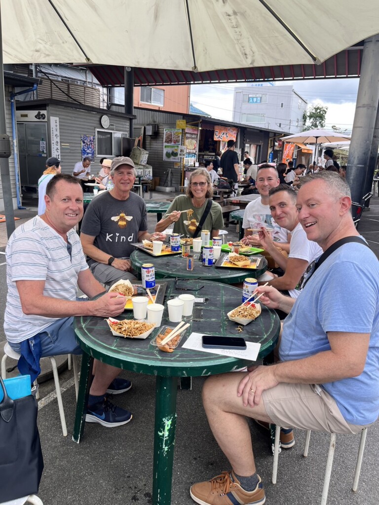 Five people enjoying lunch at outdoor tables in Omiya alley food street.