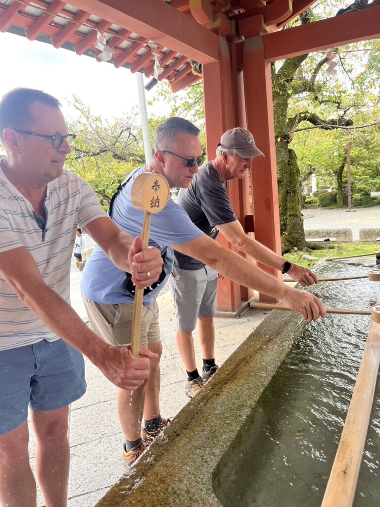 Men washing hands at a temizuya (purification station) in front of the shrine.