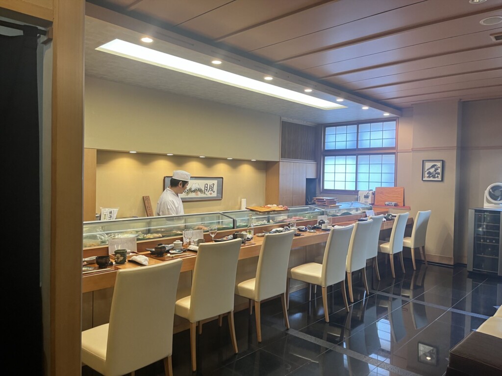 Traditional  sushi counter with fresh fish displayed in a glass case,and a skilled sushi chef preparing sushi behind the counter in Fuji City. 
