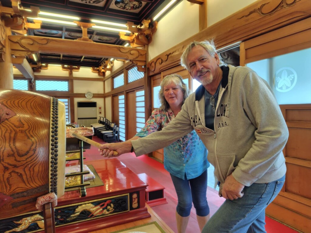 A male tour guest playing a large traditional taiko drum inside a Japanese Buddhist temple during a private tour.


