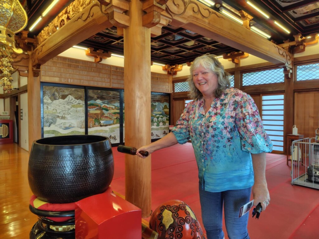 A female tour guest joyfully ringing a large Japanese Buddhist bell (orin) inside Ryugeji Temple during a cultural experience.