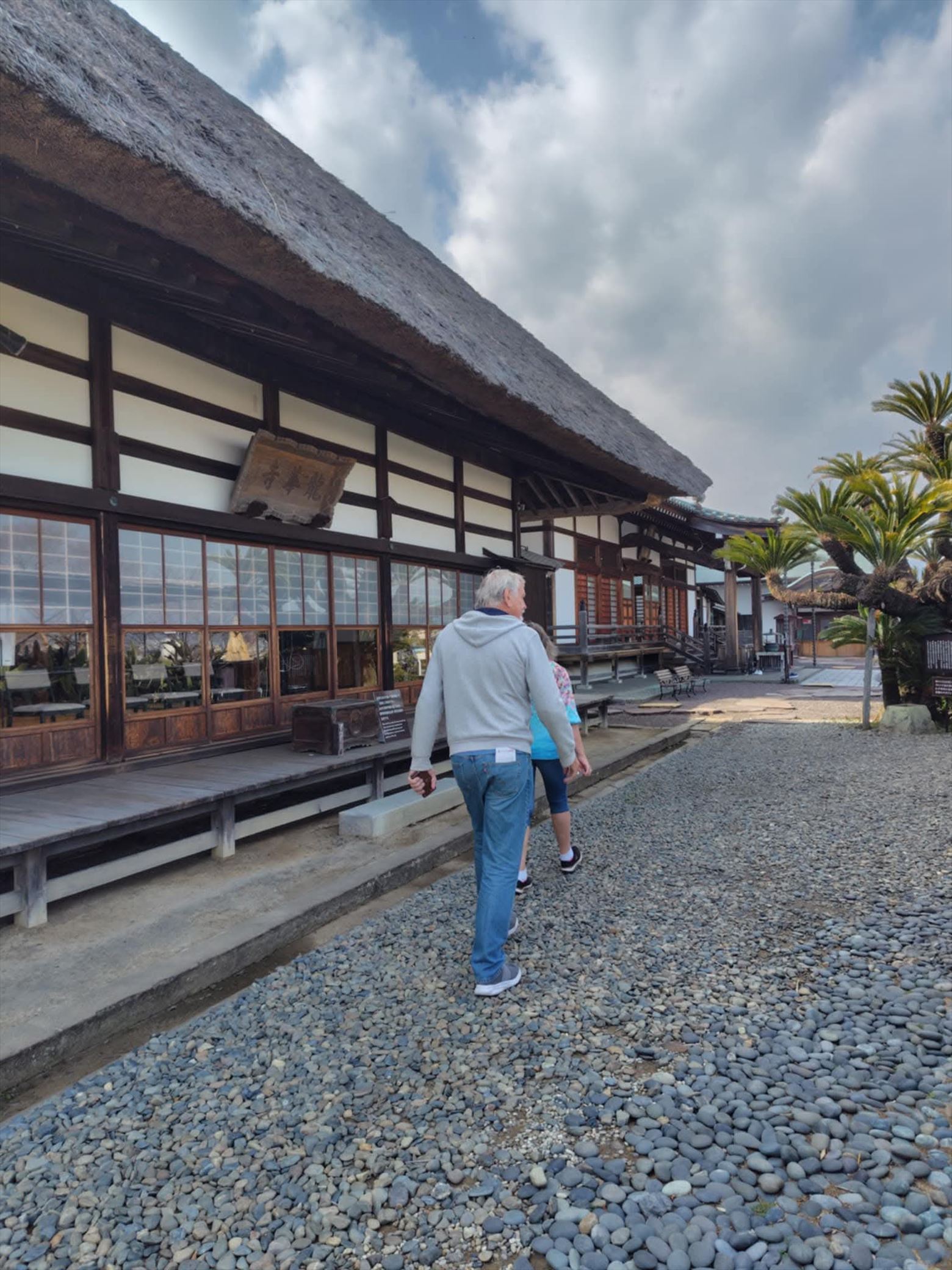 A man walking peacefully in front of the thatched-roof main hall at Ryugeji Temple, immersed in the tranquil atmosphere.