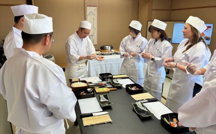 Participants wearing white sushi shef coats,making sushi during a hands-on experience in Fuji City.