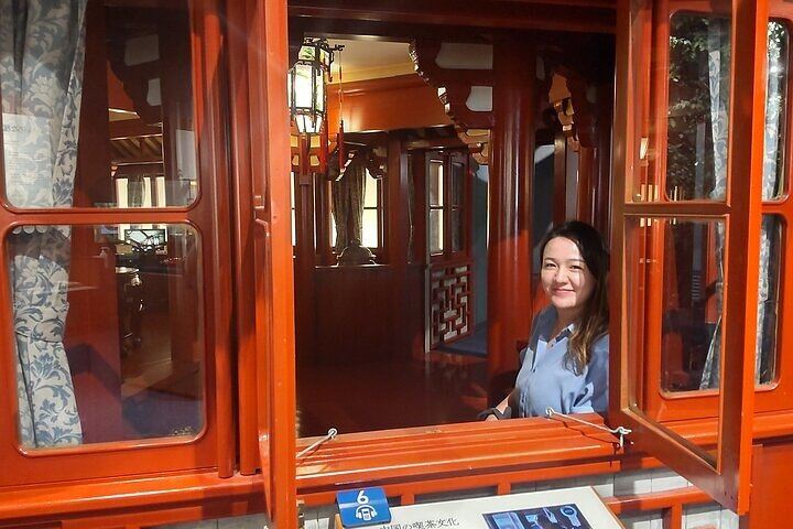 Inside a traditional-style Chinese tea house replica with a female visitor seated by the window, experiencing authentic tea culture.